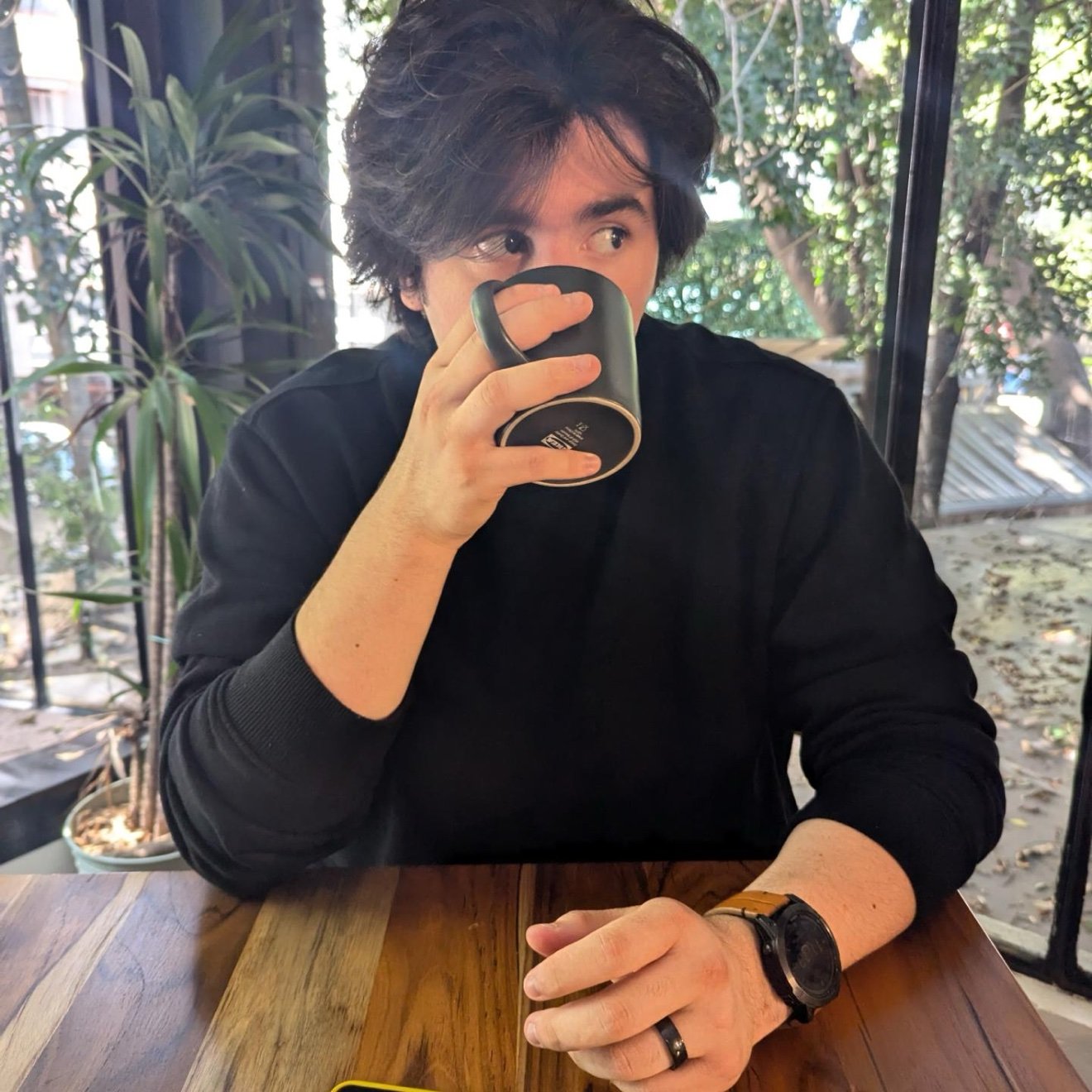 Axel drinking from a mug at a cafe, glancing sideways