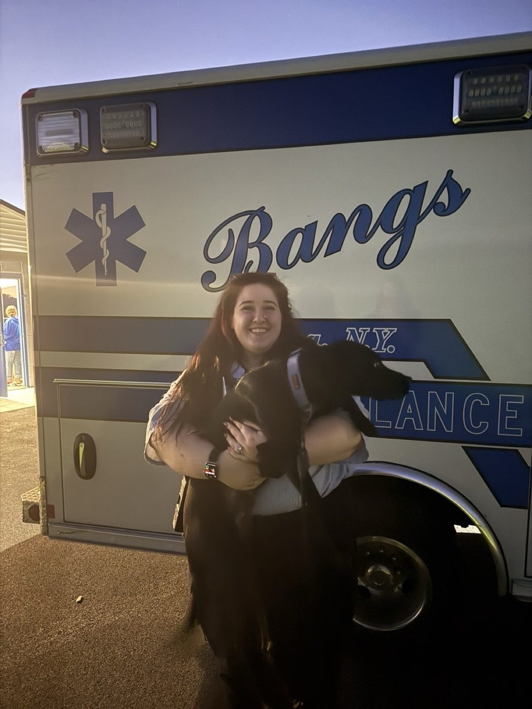 Savannah smiling and holding a black dog in front of a Bangs ambulance