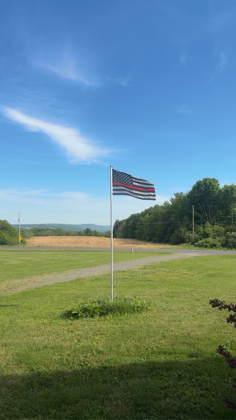 A thin red line American flag flying over a green field